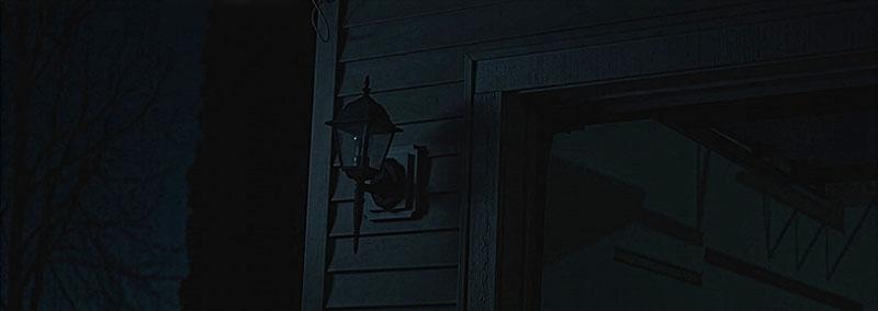 A dimly lit exterior wall of a house with a light fixture.